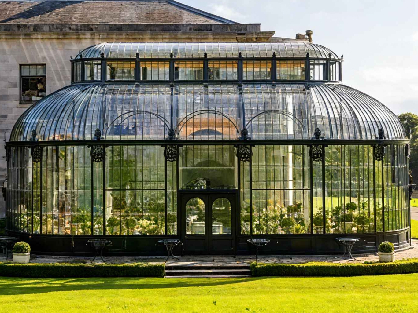 Black cast iron frame Victorian greenhouse, double dome curved tempered glass sunroom attached to historic mansion, luxury garden conservatory